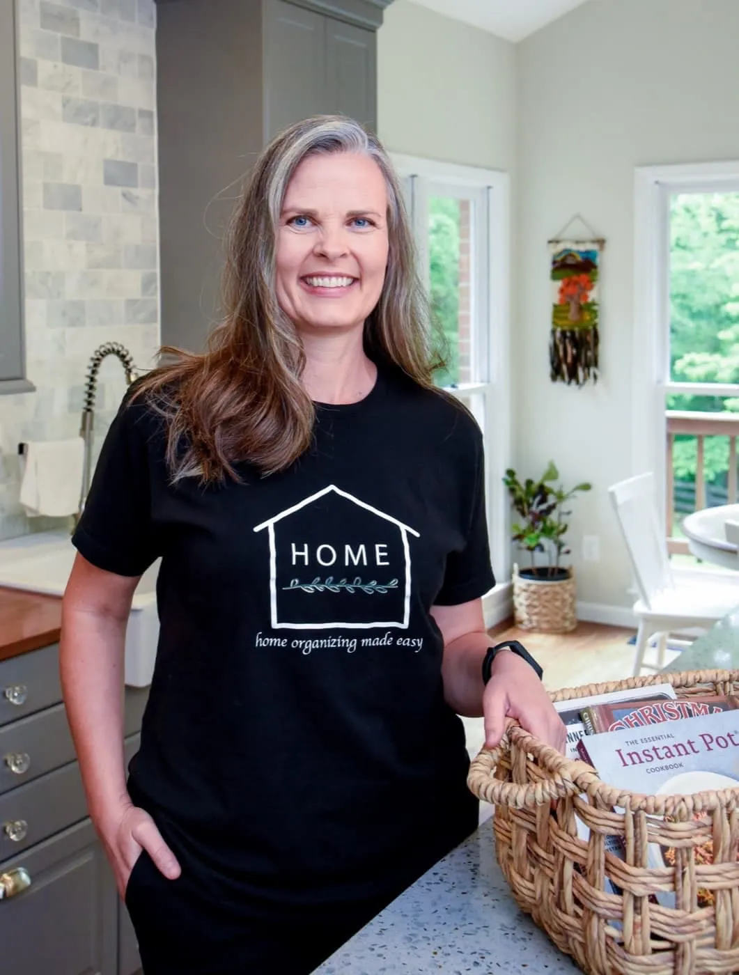 Meredith Holman, owner of Home Organizing Made Easy, holding a basket of cookbooks in an organized kitchen