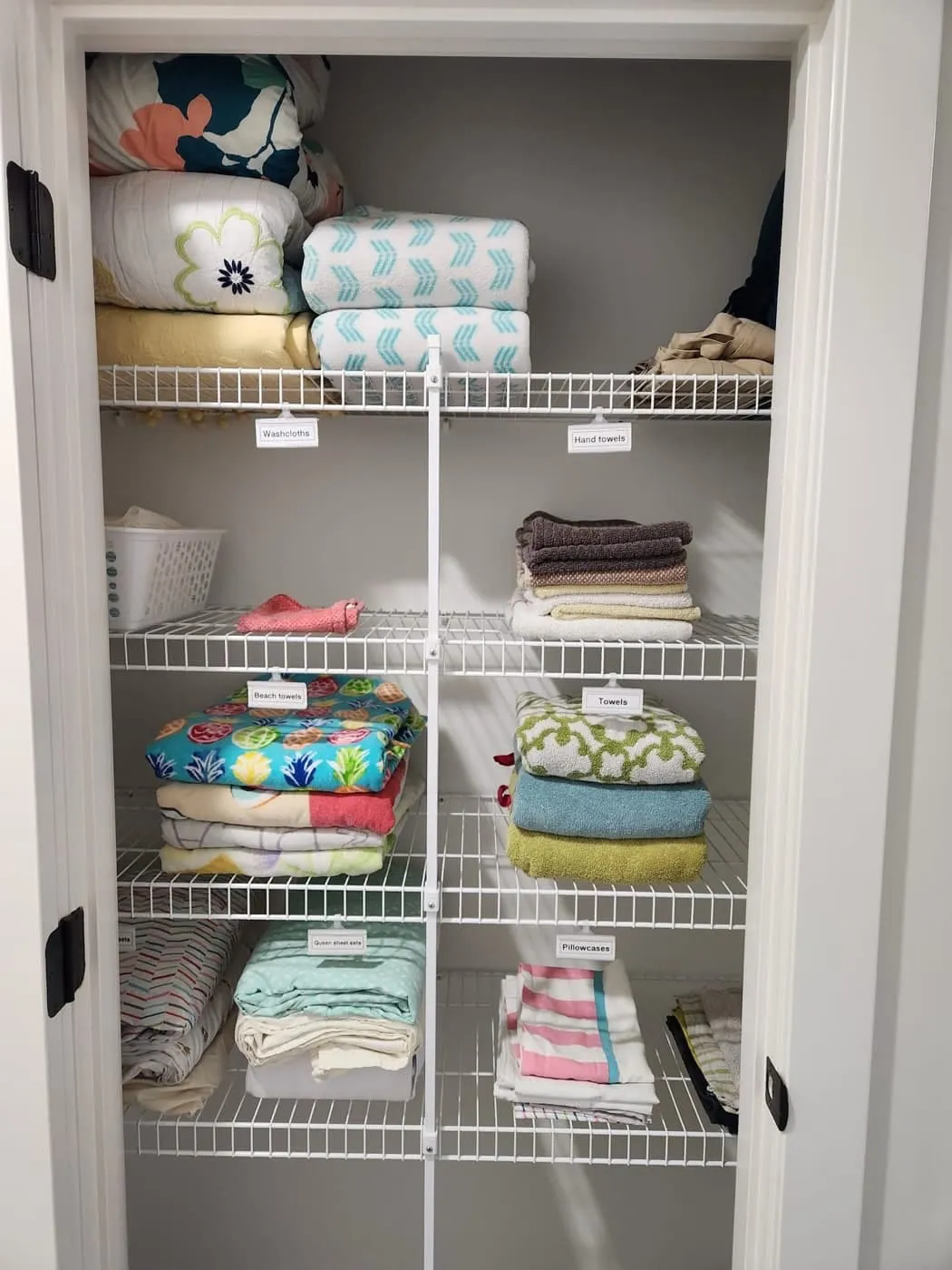 A labeled linen closet with folded towels and bedding